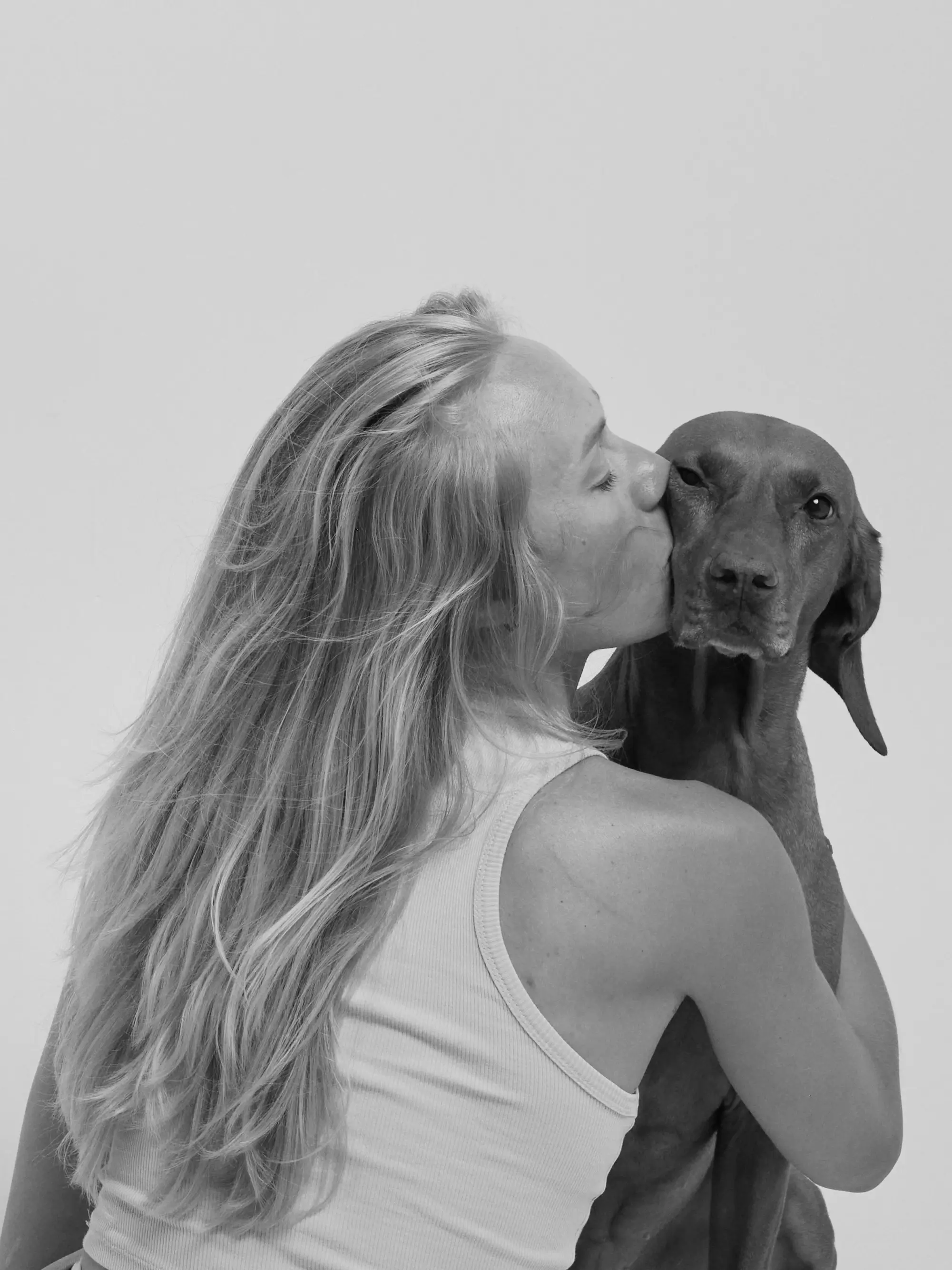 a woman kissing her dog on the cheek, white background