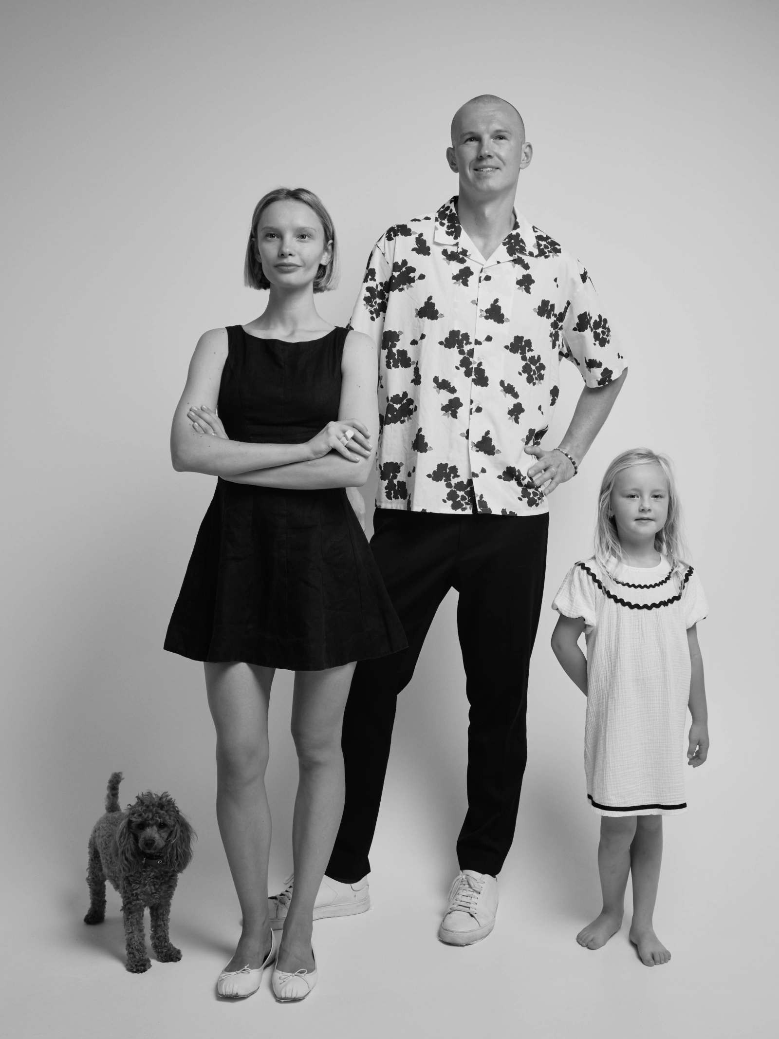 a woman, a man and a child standing with a small poodle, white background