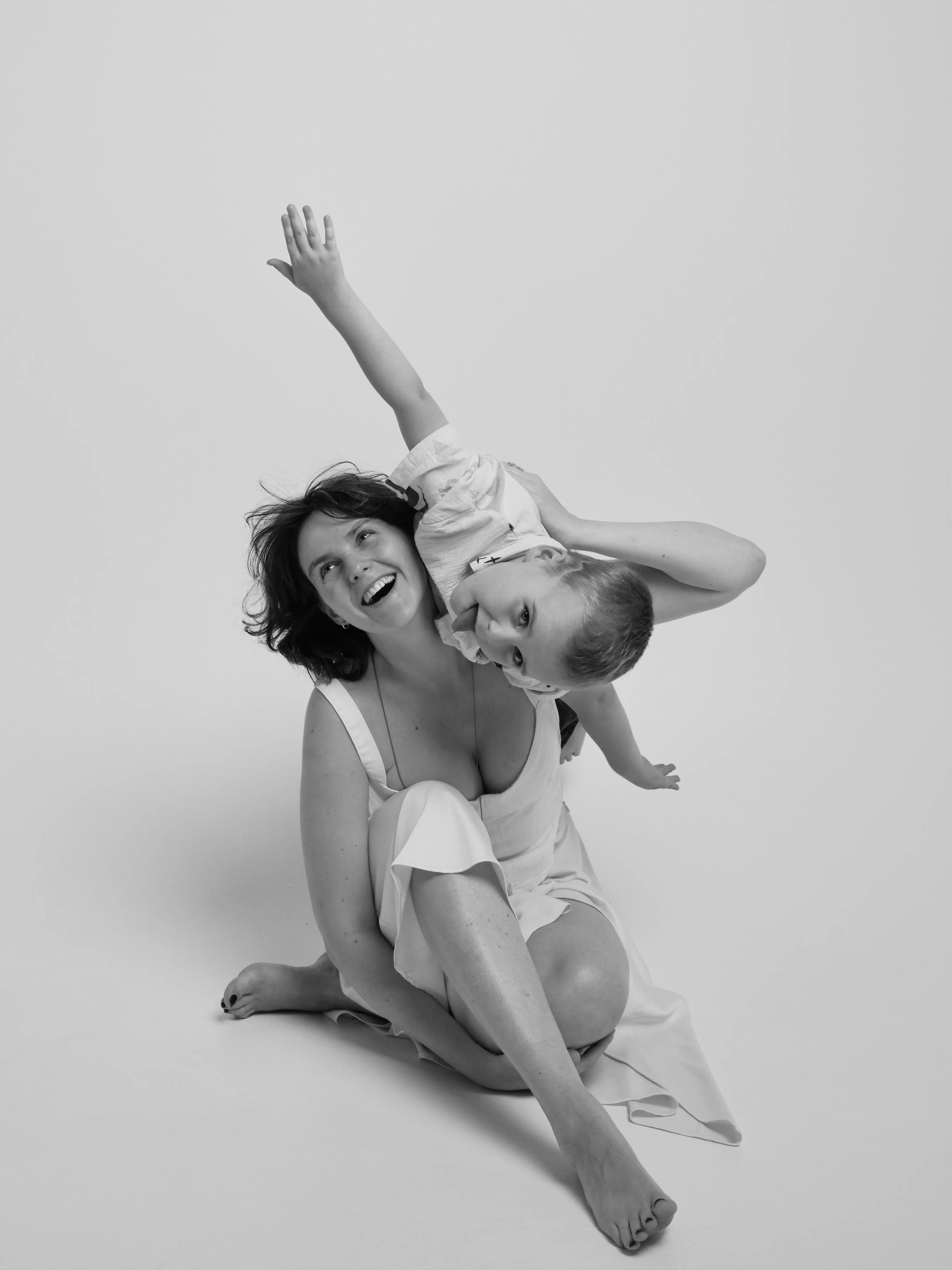 a woman sitting on the floor laughing with a small child on her back, white background