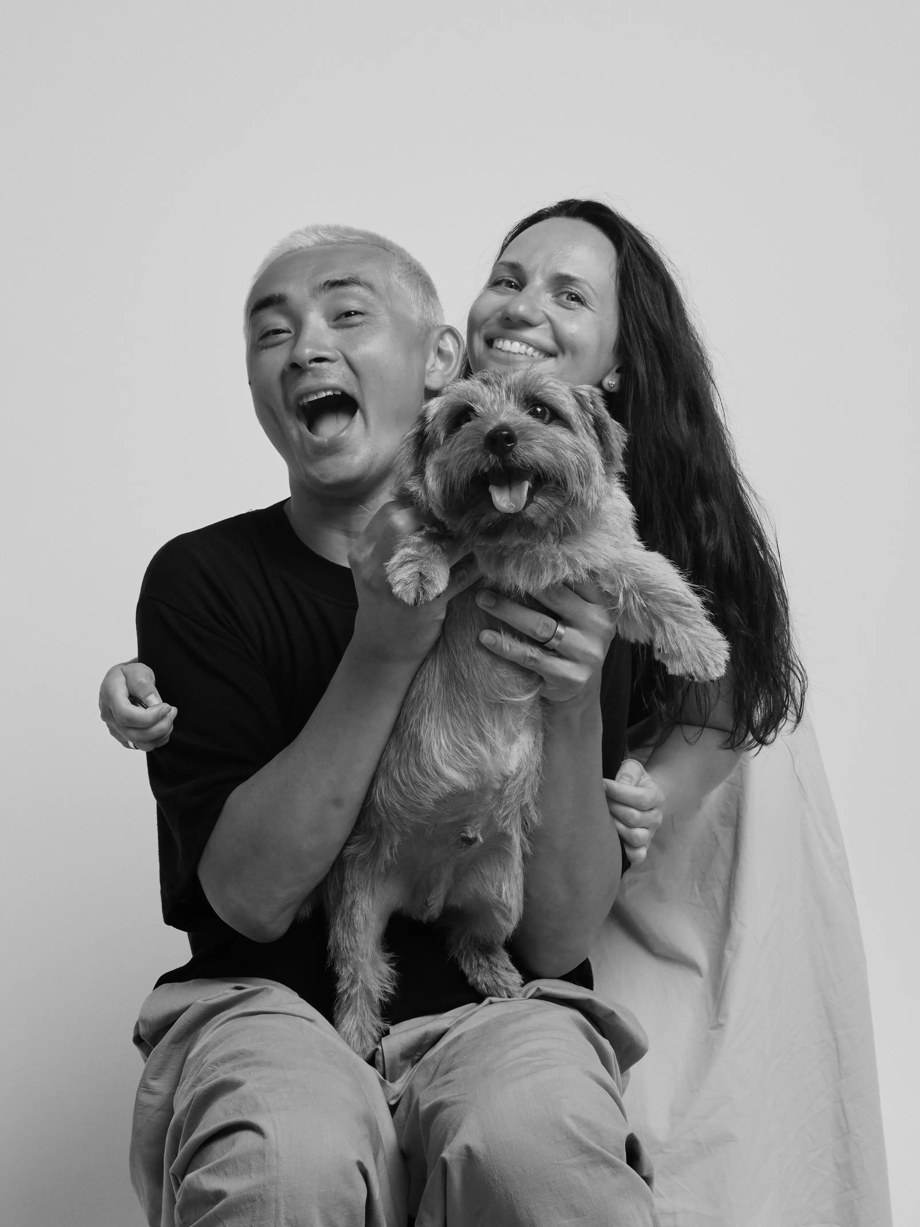 two people laughing and holding a small dog, white background