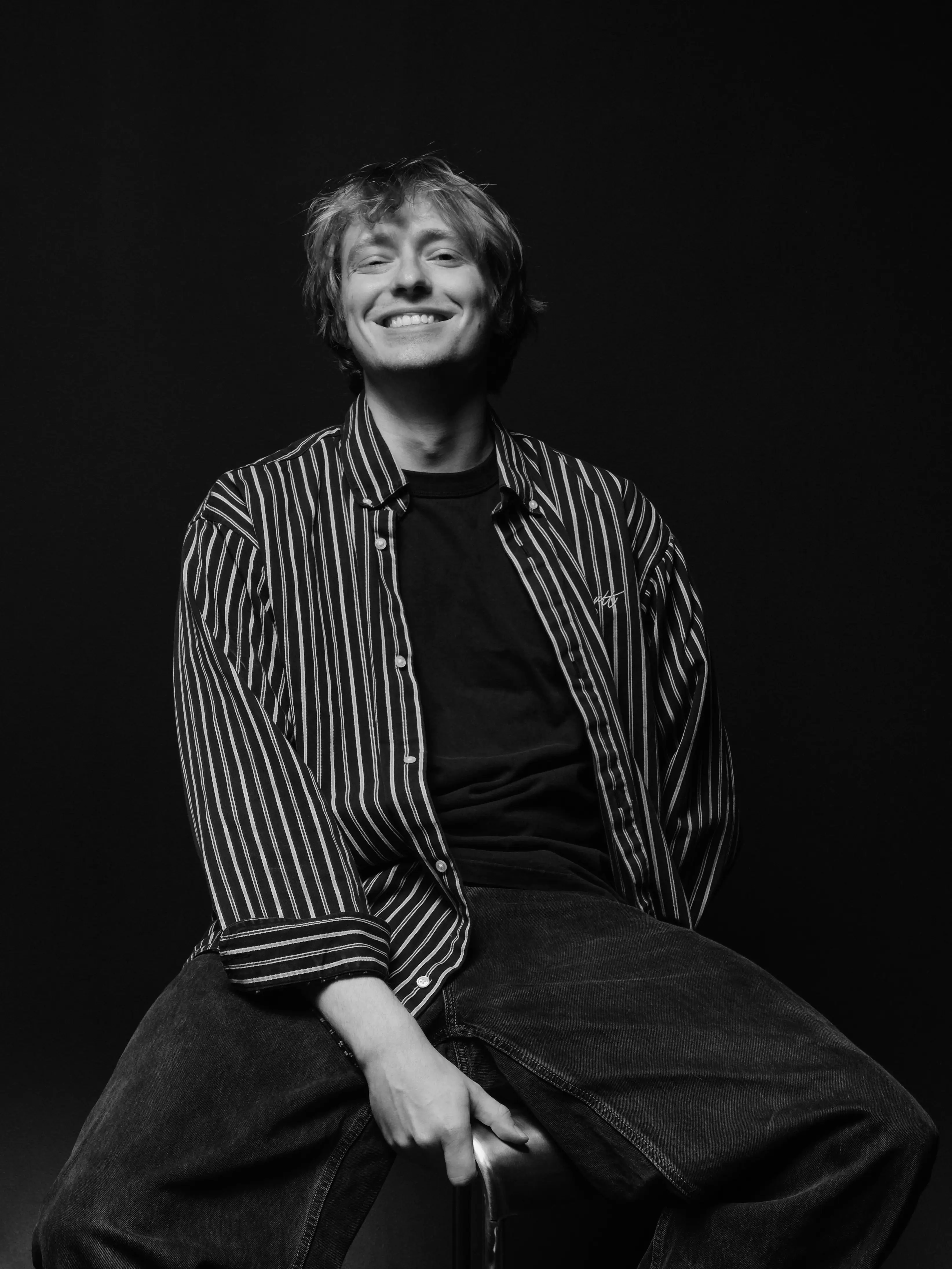 a man smiling, sitting in a striped shirt, black background