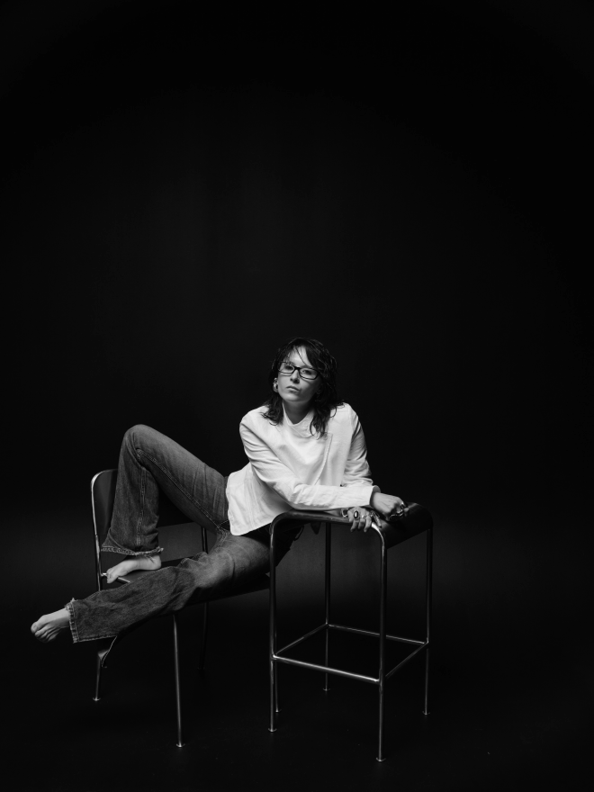 a woman in a white shirt draped across two chairs, black backdrop